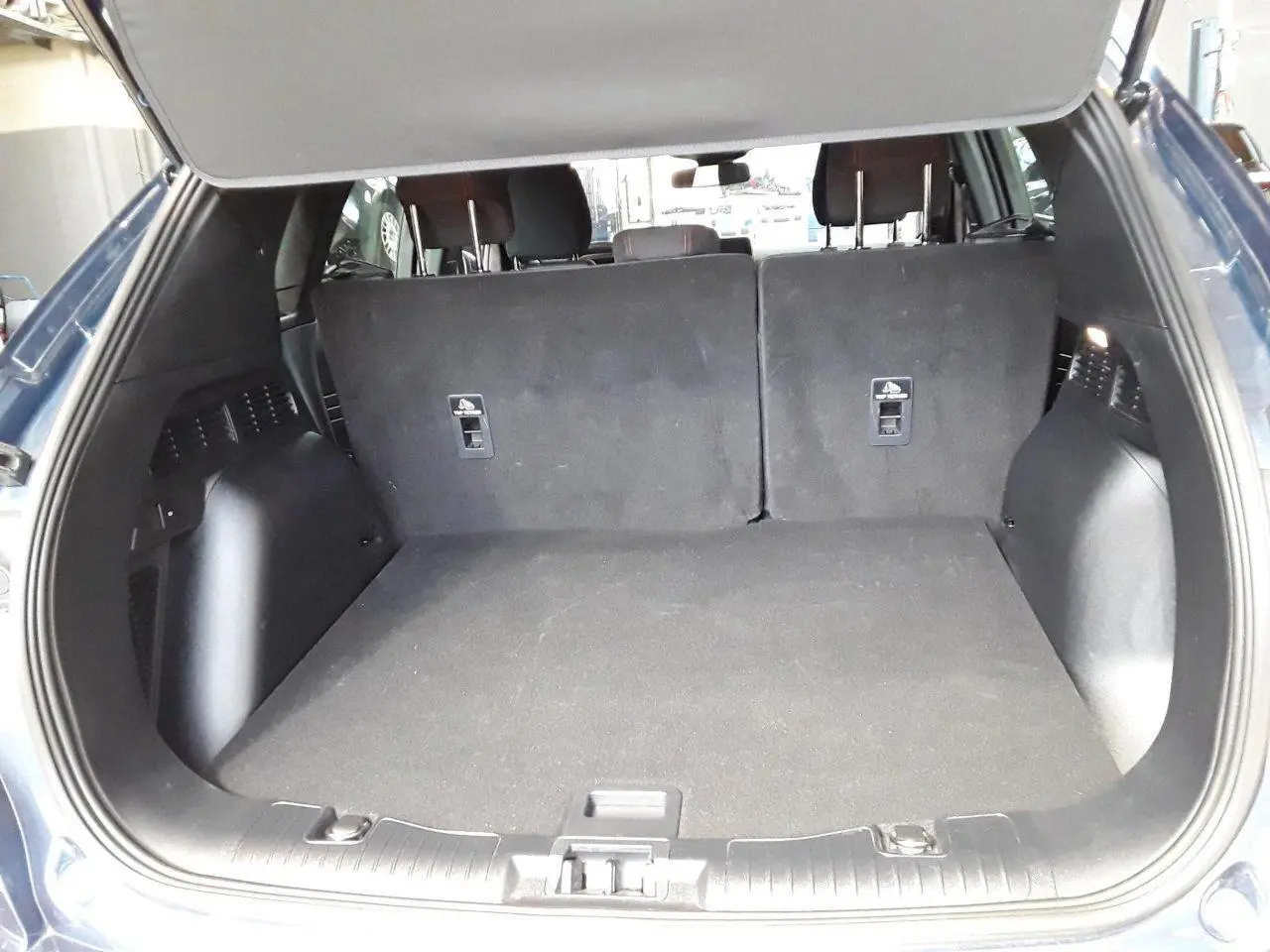 Coffre ouvert vu de l'arrière d'un Ford Kuga bleu azur 2024, montrant l'espace de chargement et les dossiers arrière rabattus.