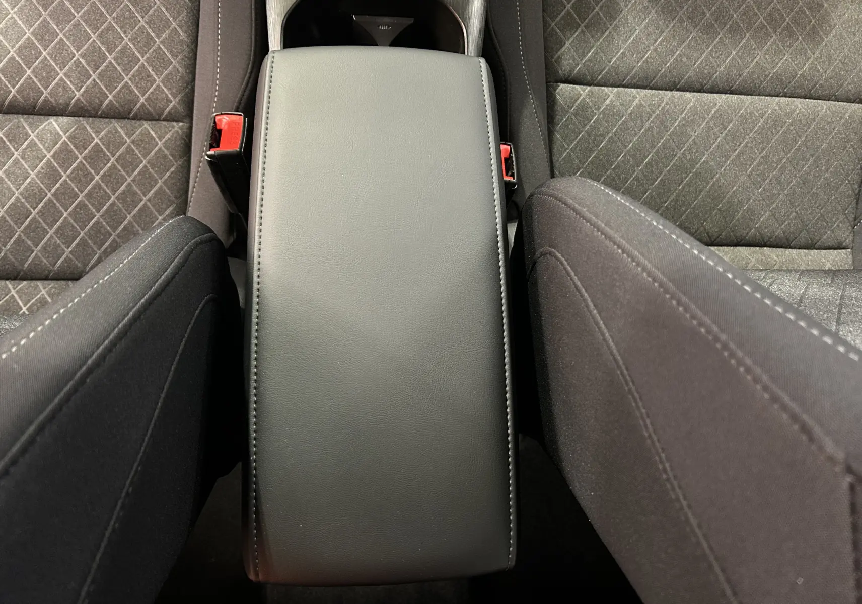 Vue plongeante sur l'accoudoir central noir entre les sièges avant en tissu gris à motifs du MG ZS Hybrid+ 2025.