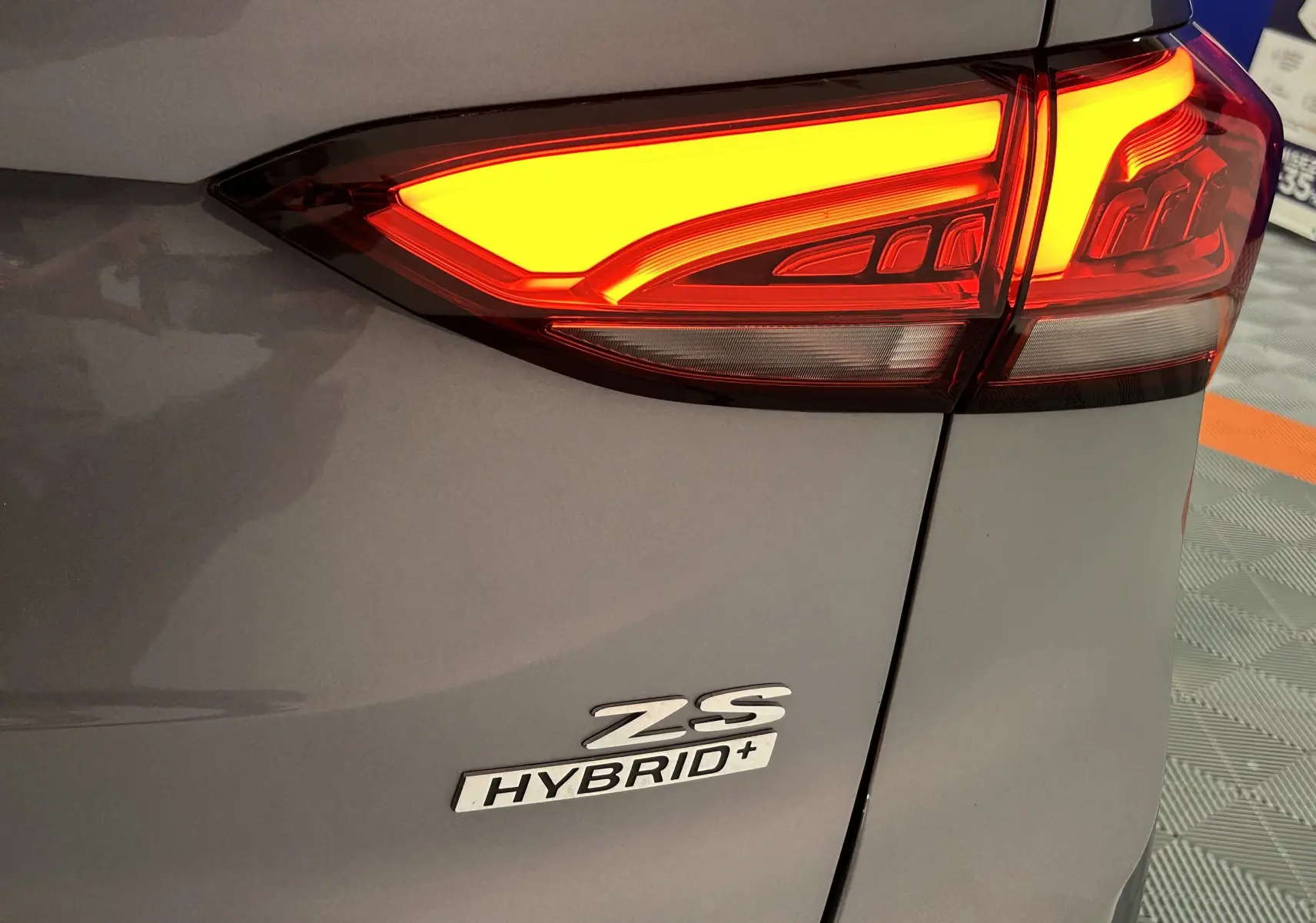 Gros plan sur le feu arrière droit allumé et le logo ZS Hybrid+ sur la carrosserie gris Hampstead du MG ZS 2025.