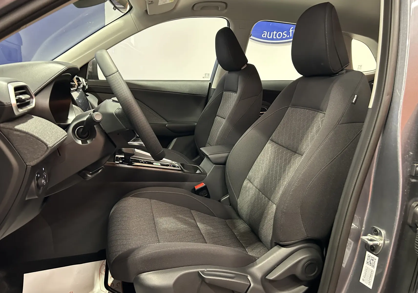 Vue intérieure côté conducteur du MG ZS Hybrid+ 2025 en Hampstead Grey, sièges tissu noir avec volant chauffant.