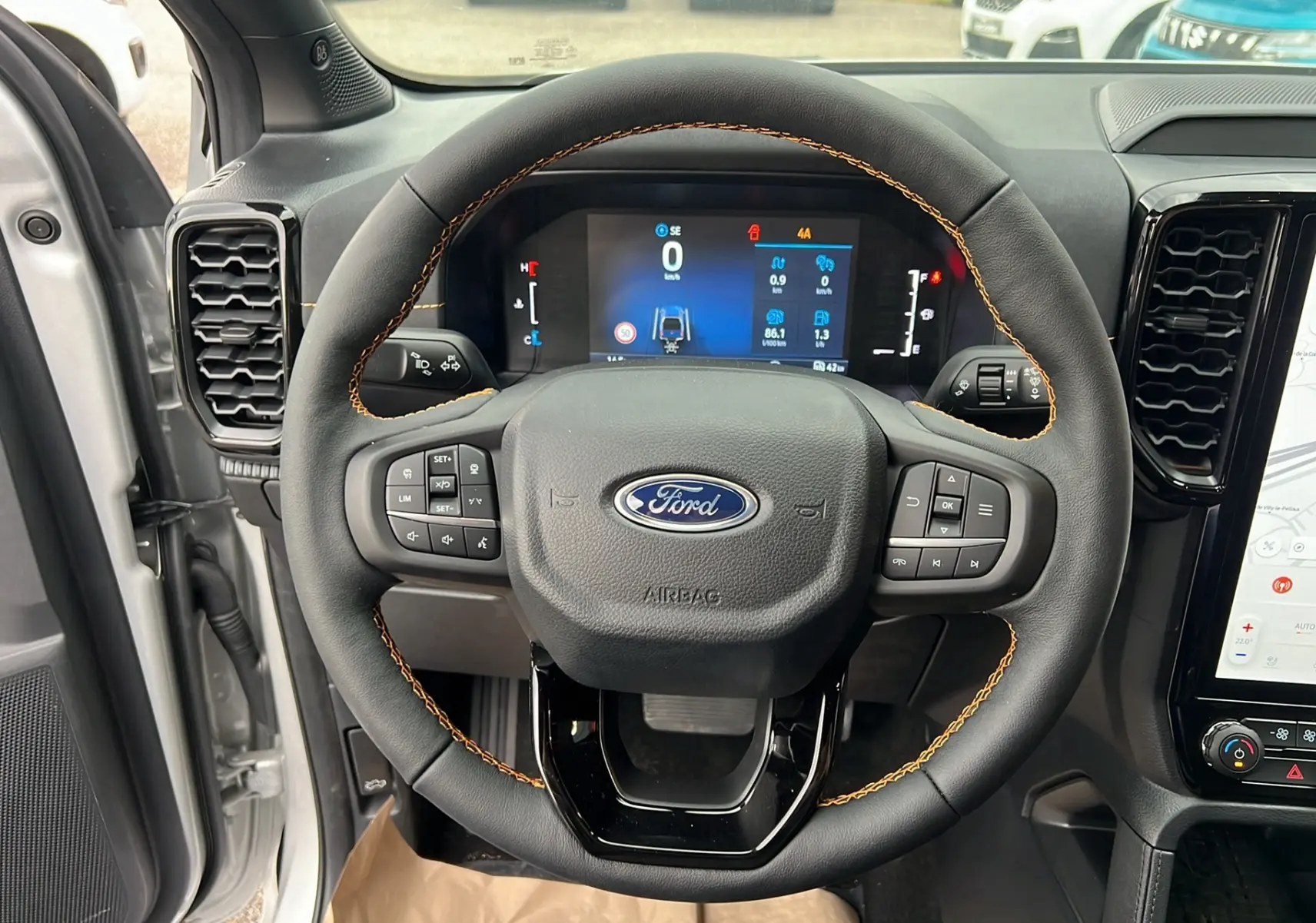 Vue intérieure centrée sur le volant cuir noir avec surpiqûres orange du Ford Ranger 2025, tableau de bord numérique et écran tactile.
