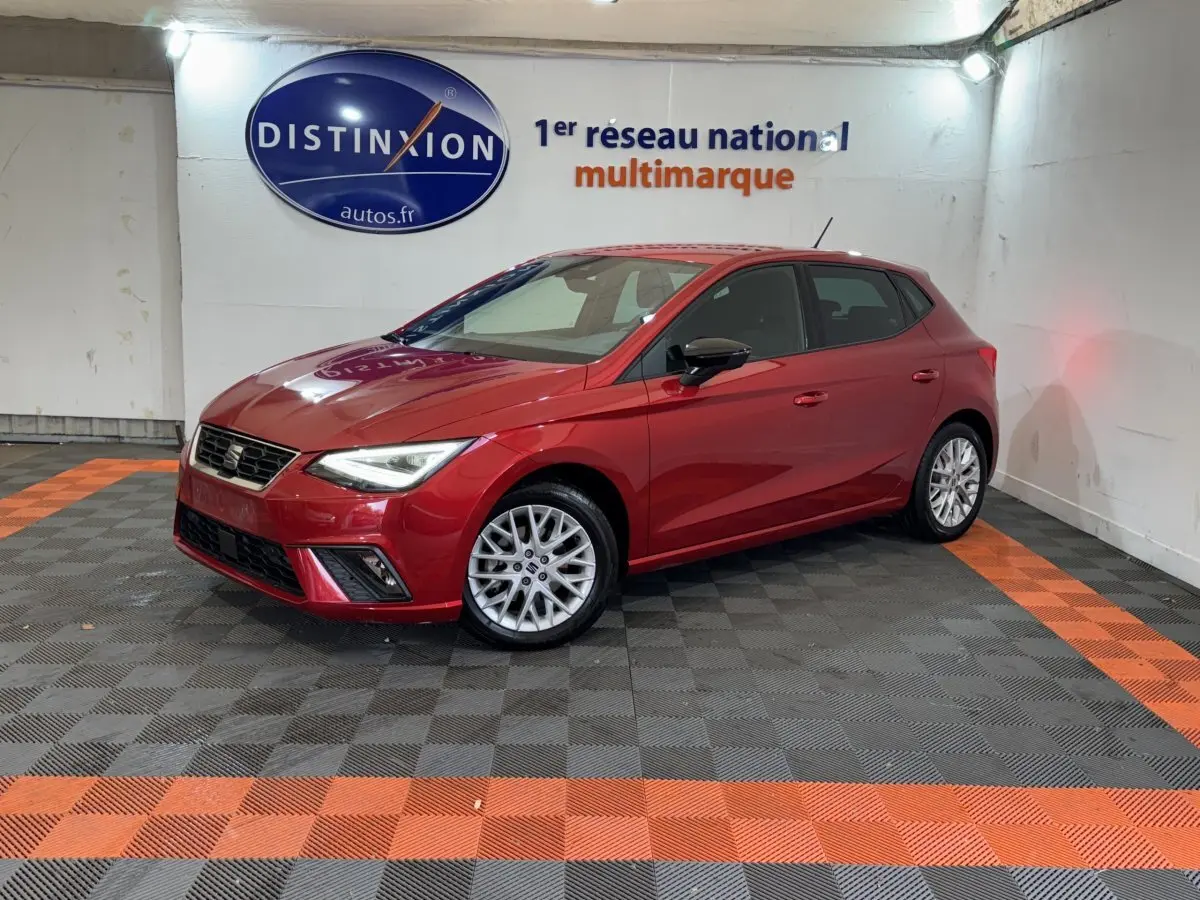 SEAT Ibiza 1.0 TSI 110 FR rouge vue 3/4 avant droit dans un showroom avec sol gris et bandes orange.