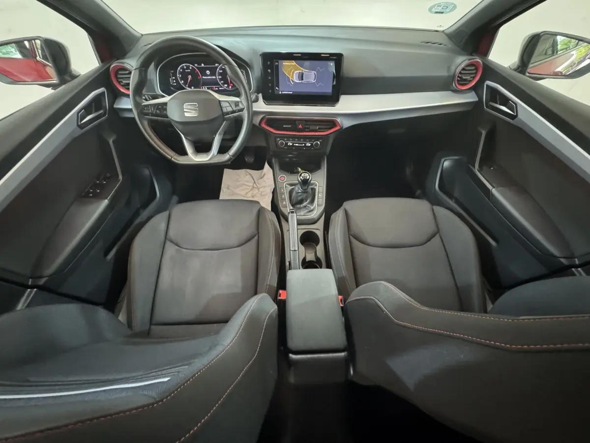 Vue intérieure avant de la SEAT Ibiza 1.0 TSI 110 FR 2024, tableau de bord noir avec touches rouges et écran tactile central.