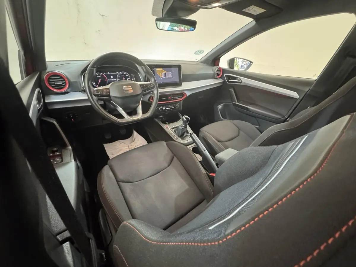Intérieur de la SEAT Ibiza 1.0 TSI 110 FR 2024 vu côté passager, volant cuir, touches rouges et écran tactile central.
