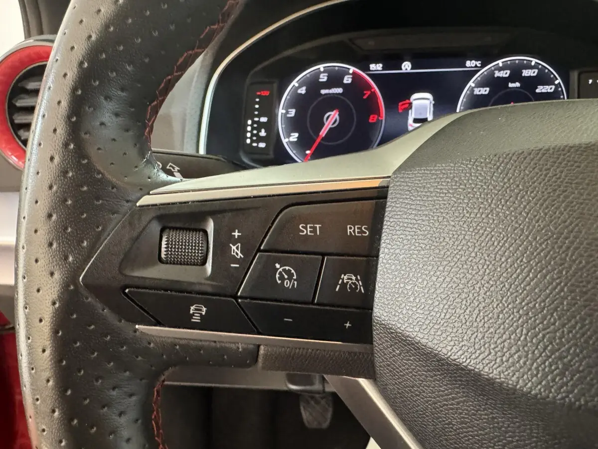 Gros plan sur le volant cuir perforé côté gauche de la SEAT Ibiza 1.0 TSI 110 FR rouge avec commandes multifonctions.