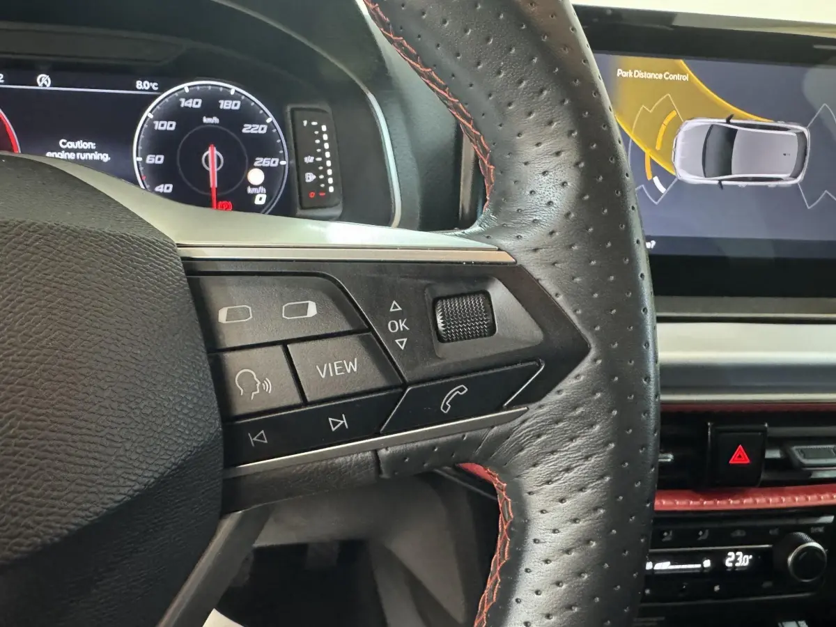 Gros plan sur le volant cuir noir avec surpiqûres rouges du SEAT Ibiza 1.0 TSI 110 FR, affichage numérique et écran tactile.