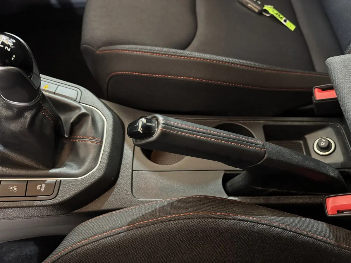 Gros plan sur la console centrale noire de la SEAT Ibiza 2024, frein à main et levier de vitesse avec surpiqûres rouges.