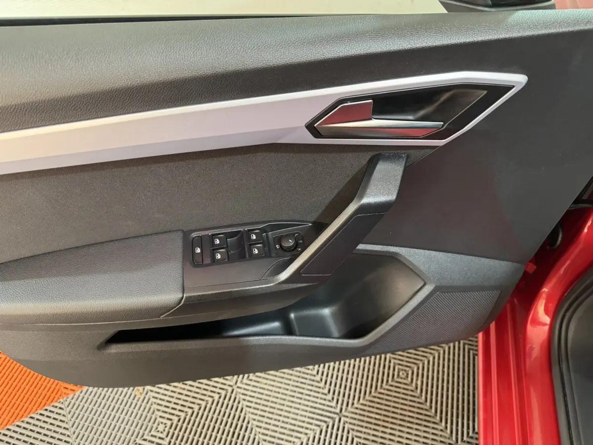 Détail de la porte côté conducteur de la SEAT Ibiza rouge 2024 avec commandes électriques et poignée argentée.