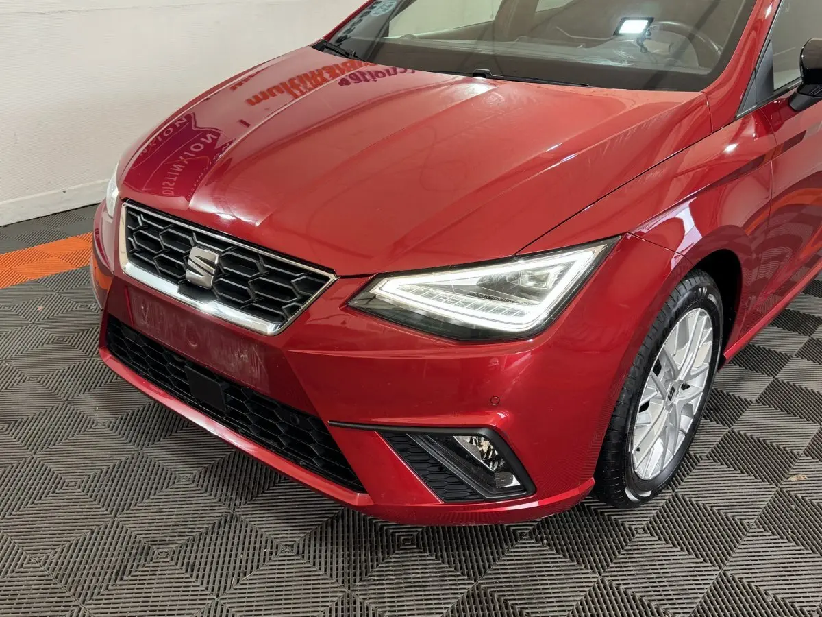 Vue 3/4 avant droit d'une SEAT Ibiza 1.0 TSI 110 FR rouge avec phares LED et jantes alliage visibles.