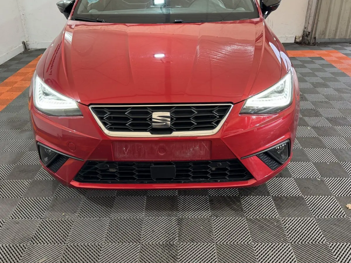 Vue avant rapprochée d'une SEAT Ibiza rouge 2024 avec phares LED allumés et calandre hexagonale noire.