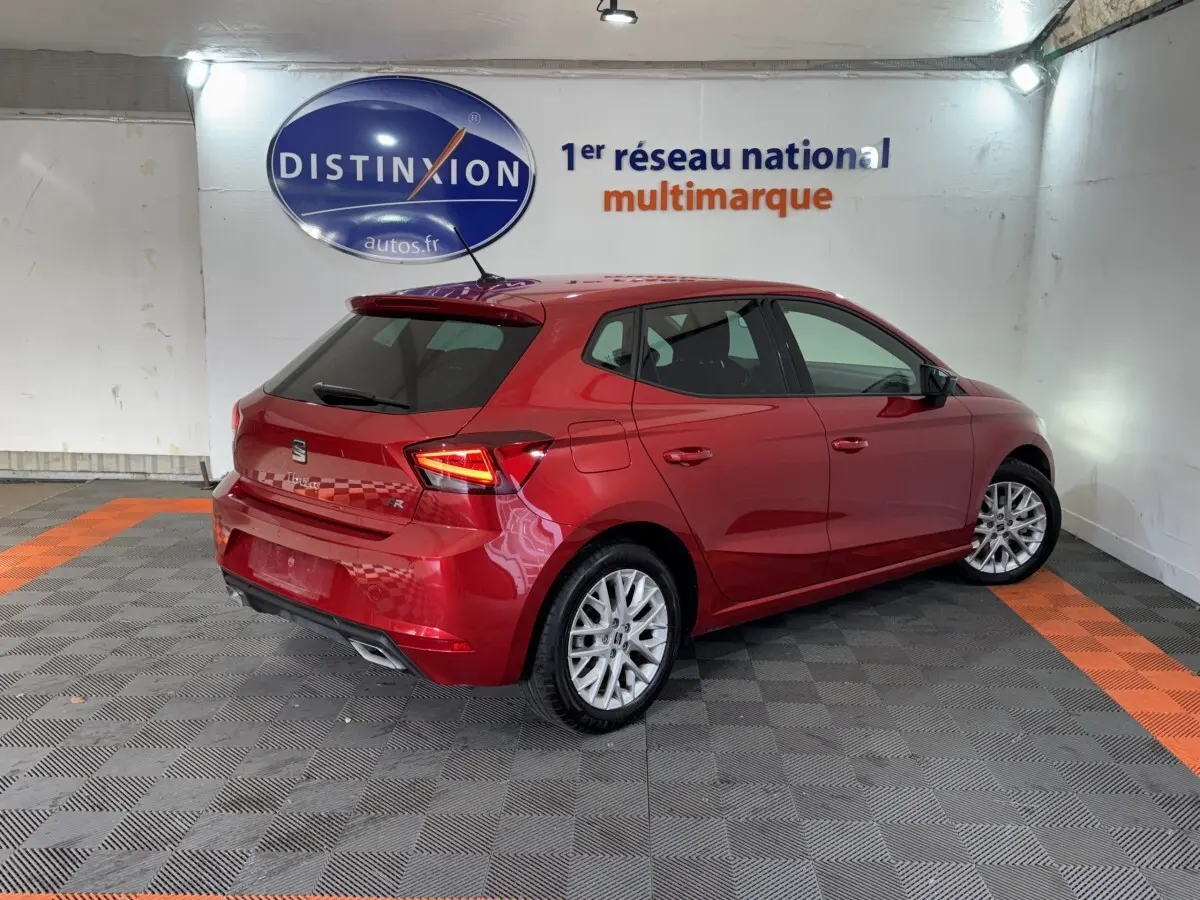 Vue 3/4 arrière droite d'une SEAT Ibiza 1.0 TSI 110 FR rouge avec jantes alliage et feux LED allumés.