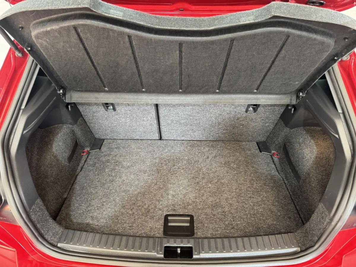 Coffre ouvert de la SEAT Ibiza 1.0 TSI 110 FR rouge, montrant l’espace de rangement et la moquette grise.