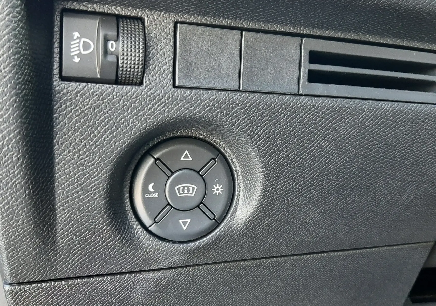 Détail du tableau de bord côté gauche de la Citroën C4 blanche, avec commande de réglage des phares et du tableau de bord.