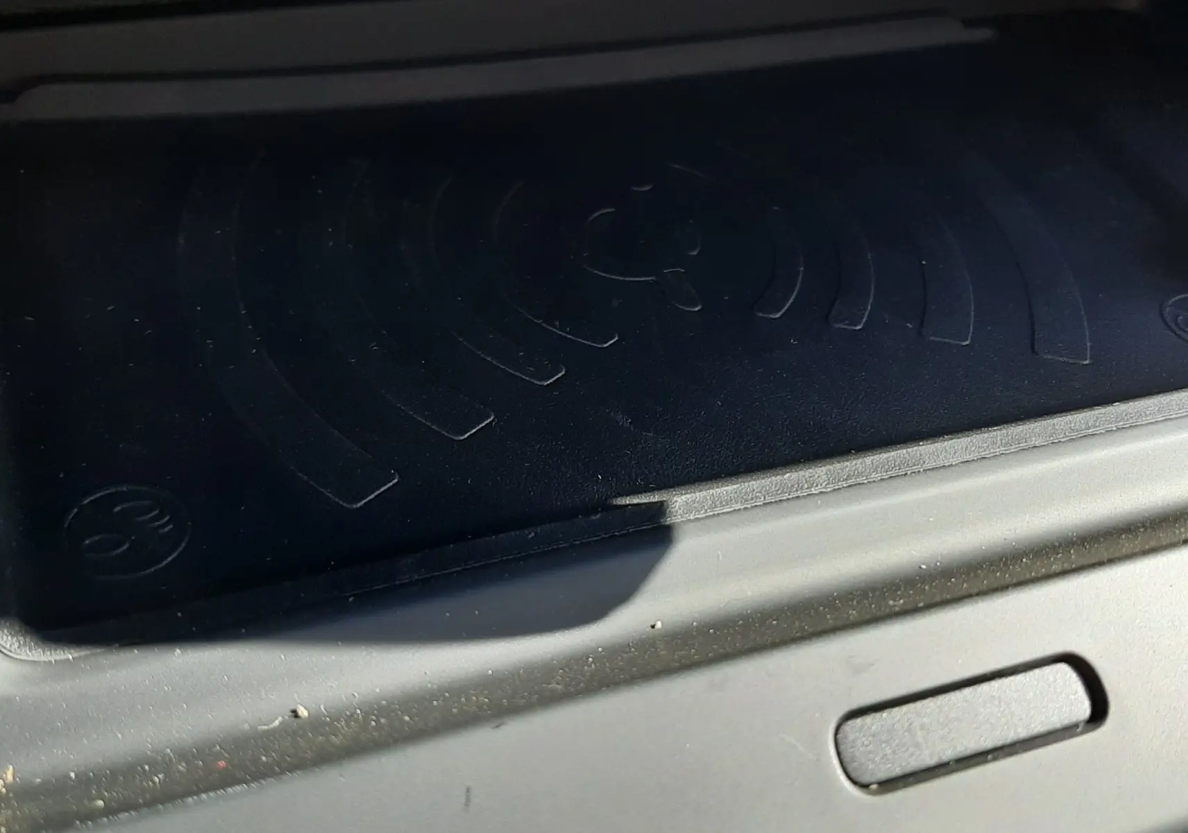 Détail de la zone de recharge sans fil noire dans l’habitacle du Citroën C4 blanc Okenite, vue rapprochée.
