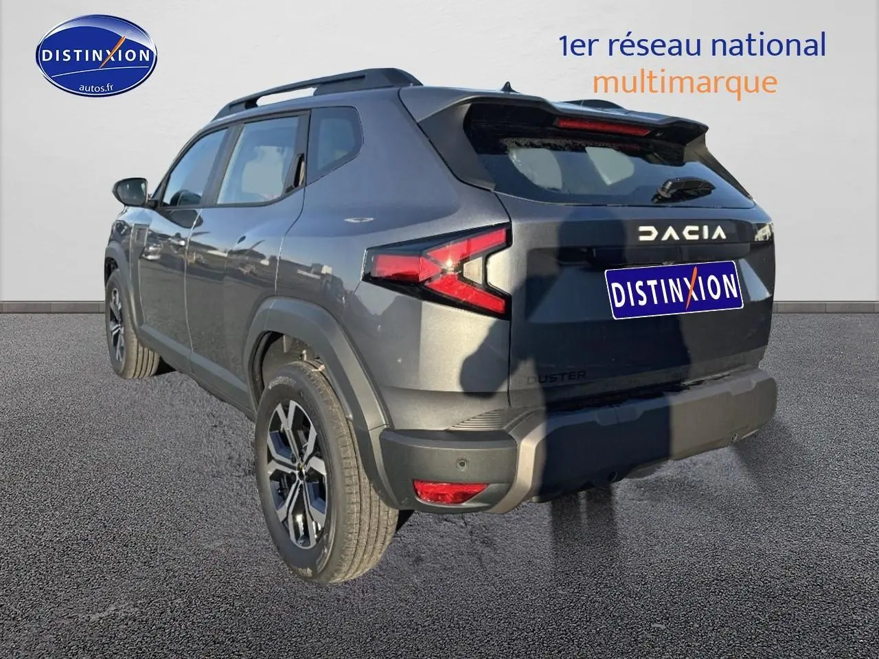 Vue 3/4 arrière droite du Dacia Duster gris schiste avec jantes alu et barres de toit visibles.