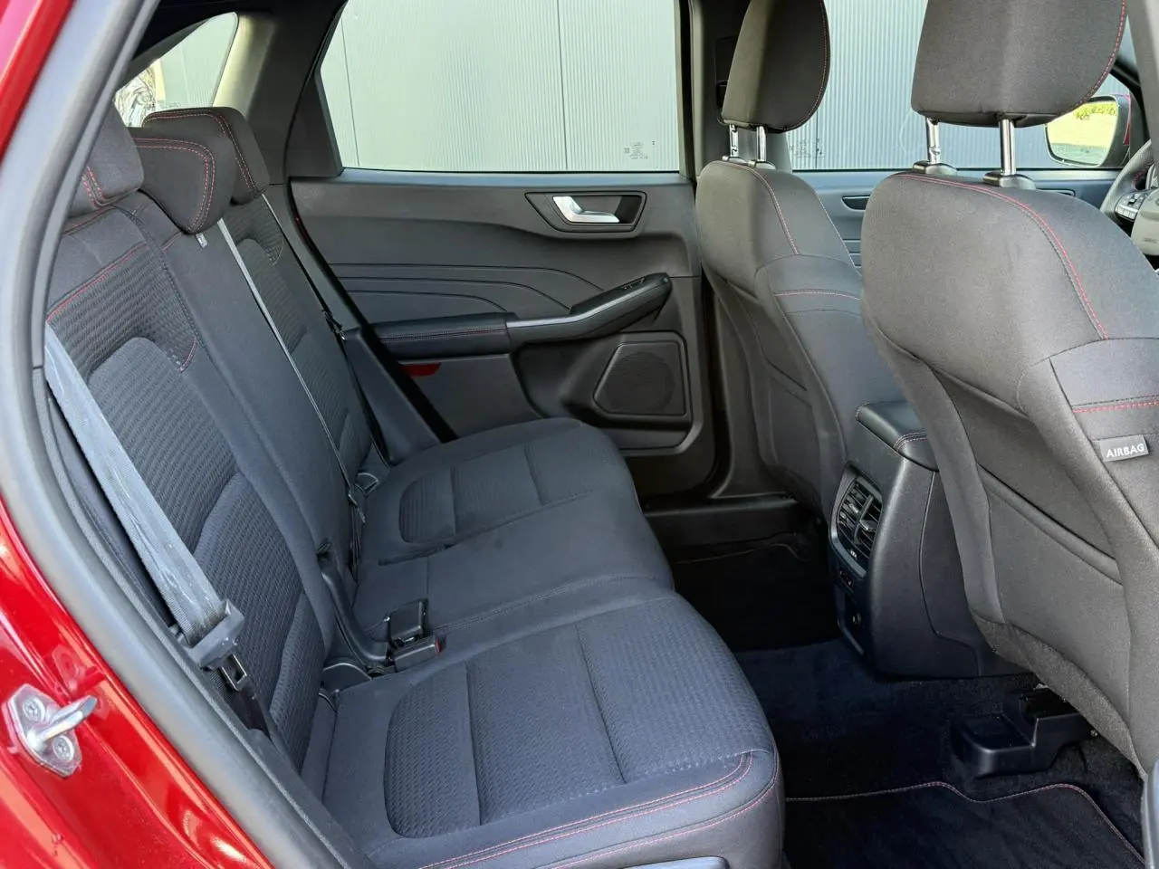 Vue intérieure arrière côté gauche du Ford Kuga rouge Lucifer 2024, sièges tissu noirs avec surpiqûres rouges.