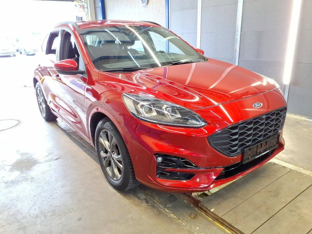 Ford Kuga rouge Lucifer vue 3/4 avant droit, avec calandre noire et jantes alliage 18 pouces en intérieur d'atelier.