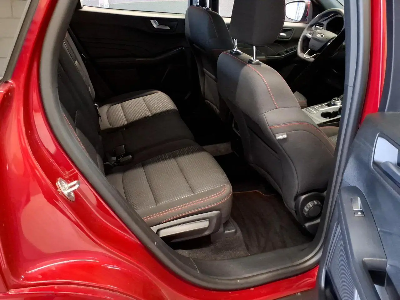 Vue intérieure côté arrière gauche du Ford Kuga rouge Lucifer 2024, sièges tissu noir avec surpiqûres rouges.