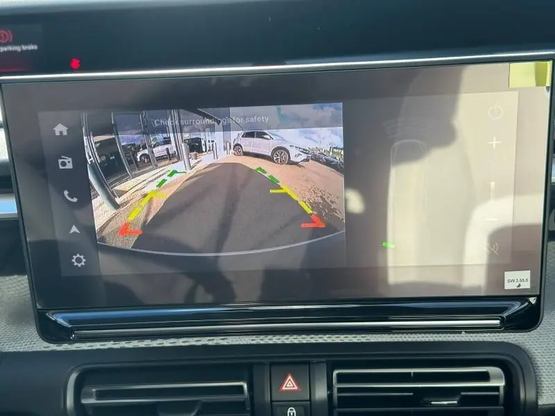 Écran tactile affichant la caméra de recul avec vue arrière sur un sol goudronné et un véhicule blanc en arrière-plan.