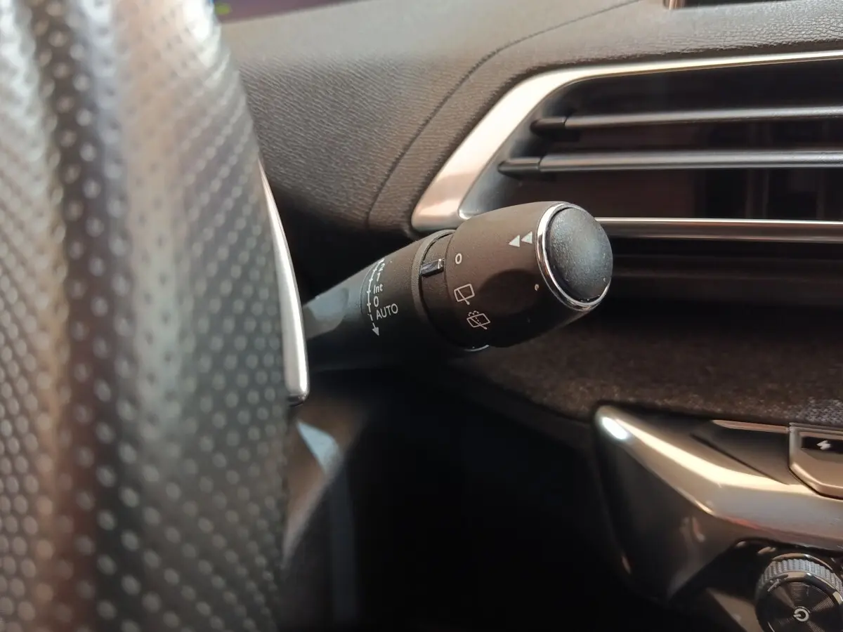 Gros plan sur la commande d’essuie-glace à gauche du volant dans l’habitacle noir du Peugeot 3008 bleu.