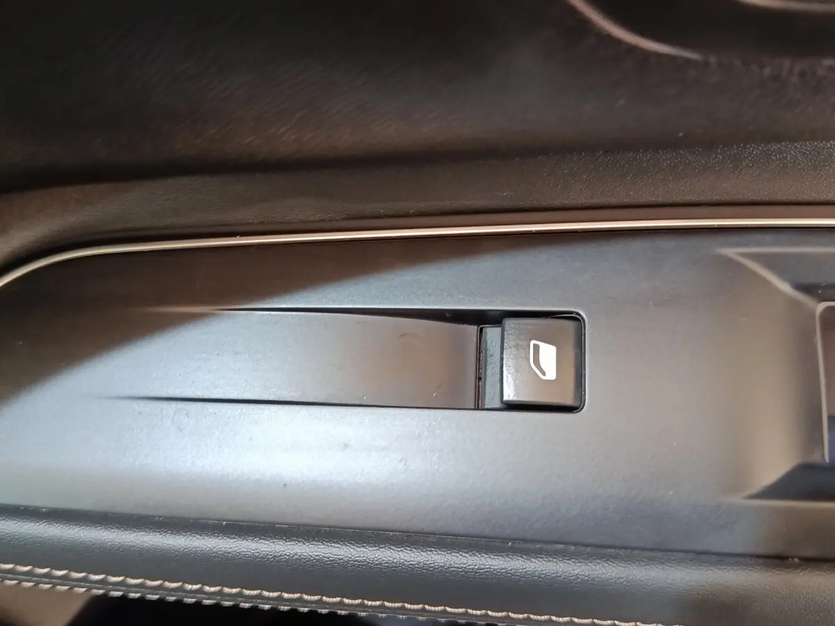 Gros plan sur le bouton de commande de lève-vitre côté conducteur dans l'intérieur noir du Peugeot 3008 hybride bleu.