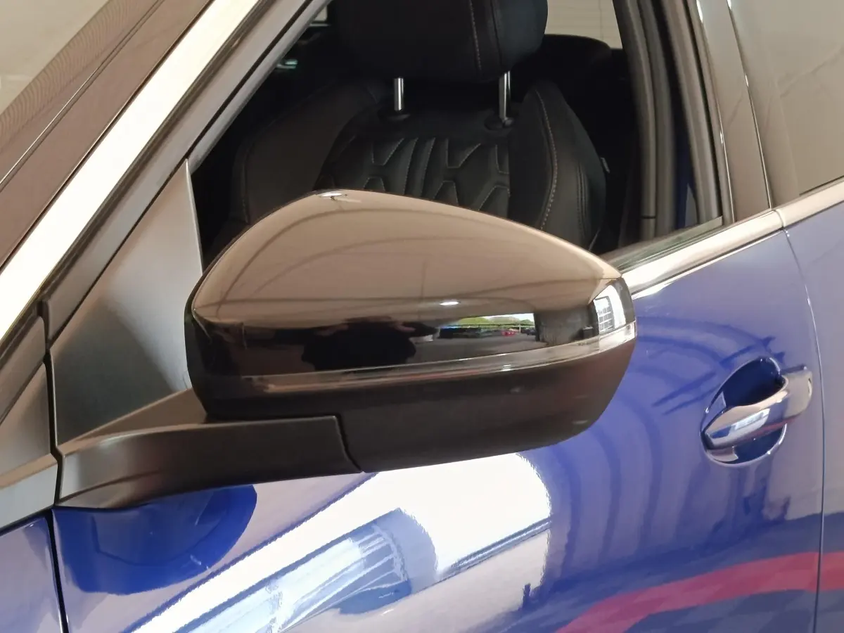 Rétroviseur noir en gros plan côté gauche sur Peugeot 3008 bleu hybride rechargeable, siège avant en cuir visible.
