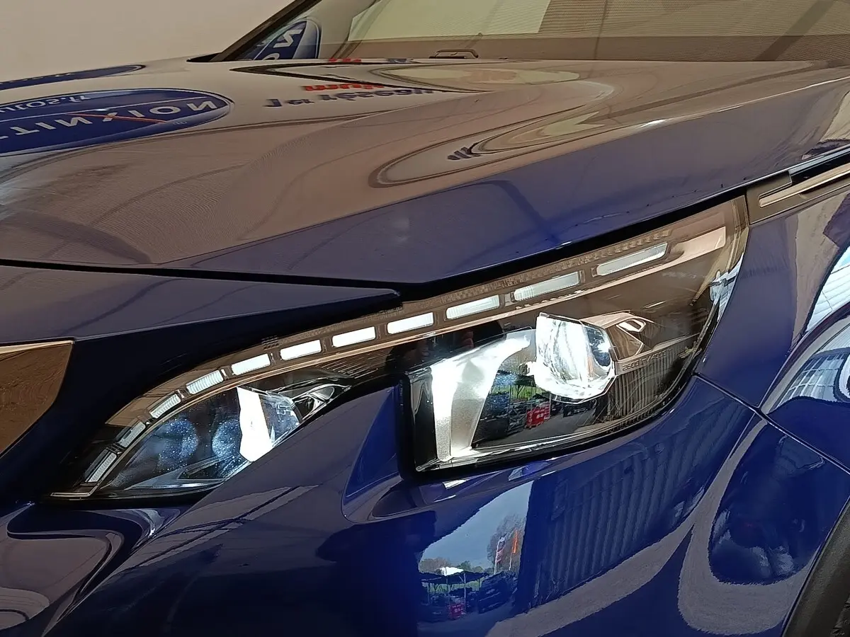 Gros plan sur le phare avant droit LED d’un Peugeot 3008 bleu, soulignant les lignes modernes et la finition brillante.