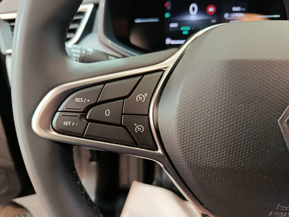 Gros plan sur le côté gauche du volant noir de la Renault Clio 2025, avec commandes de régulateur de vitesse visibles.