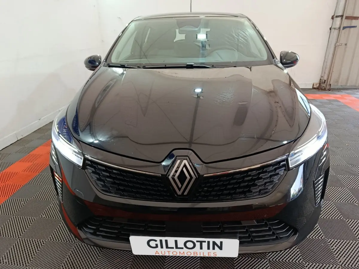 Vue avant d'une Renault Clio noire 2025 avec calandre moderne et phares LED allumés en intérieur showroom.
