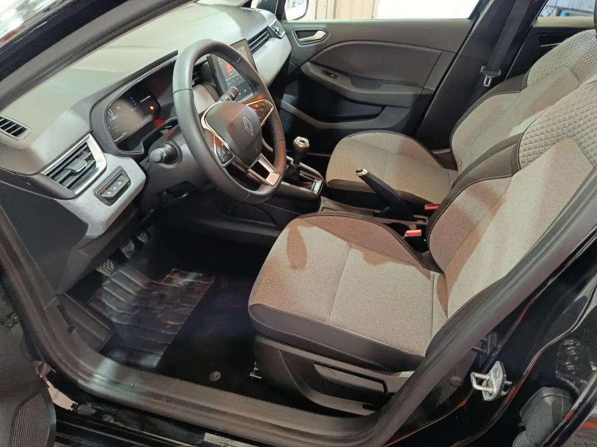 Intérieur avant droit de la Renault Clio noire 2025, montrant sièges tissu gris, volant multifonctions et boîte manuelle.