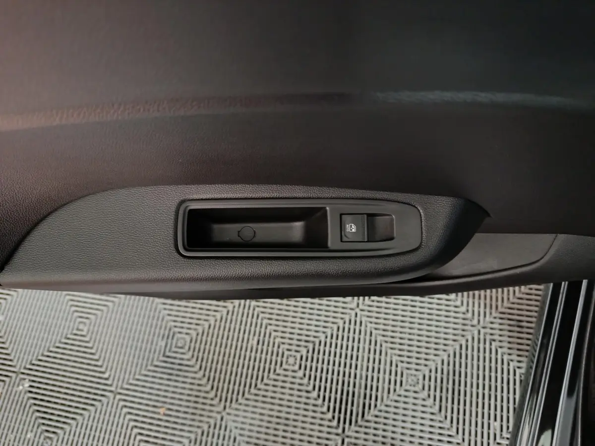 Gros plan sur la commande de lève-vitre côté conducteur de la Renault Clio noire, intérieur sombre.