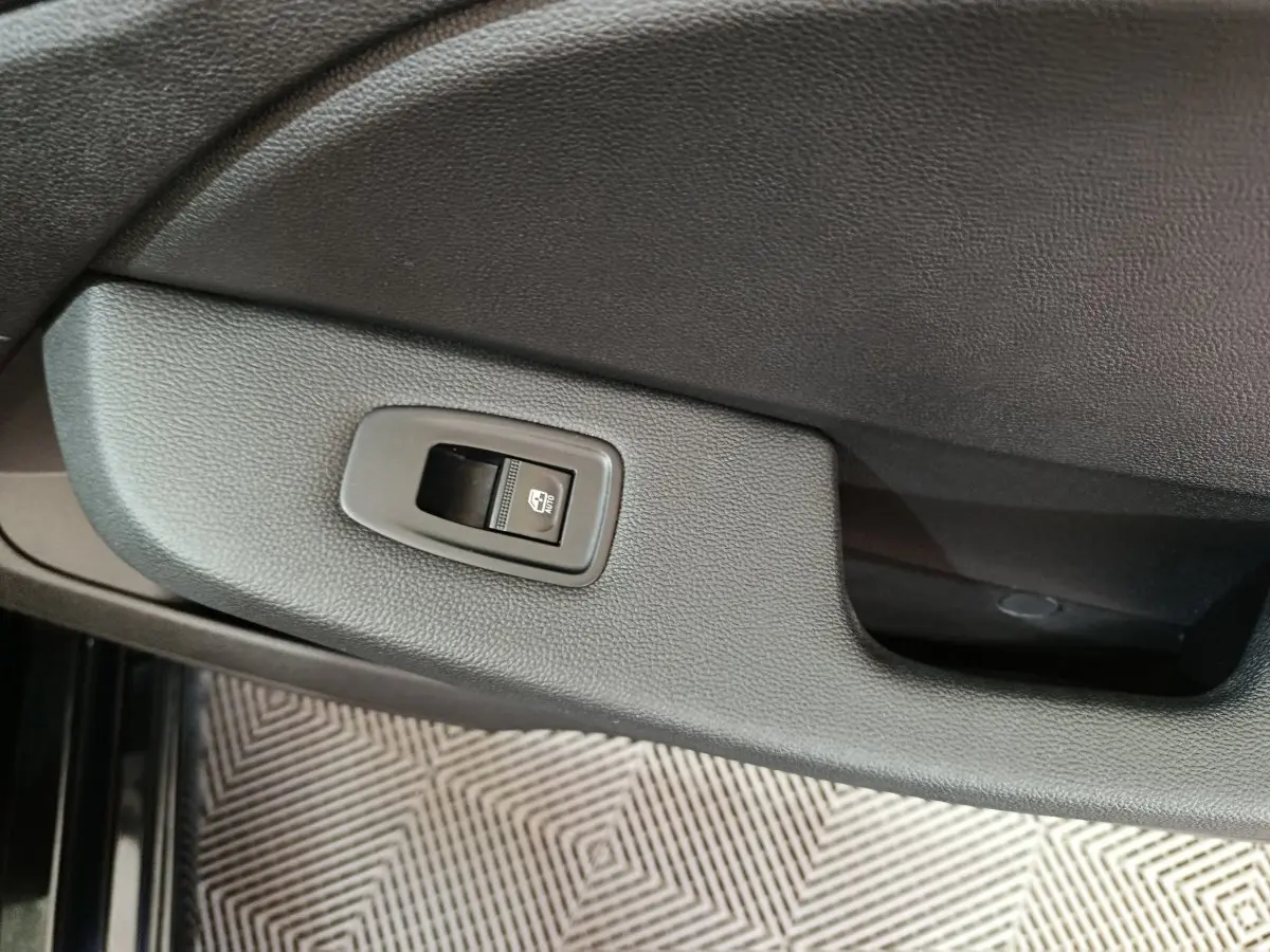 Gros plan sur le bouton de commande de la vitre électrique côté conducteur dans une Renault Clio noire, intérieur sobre.