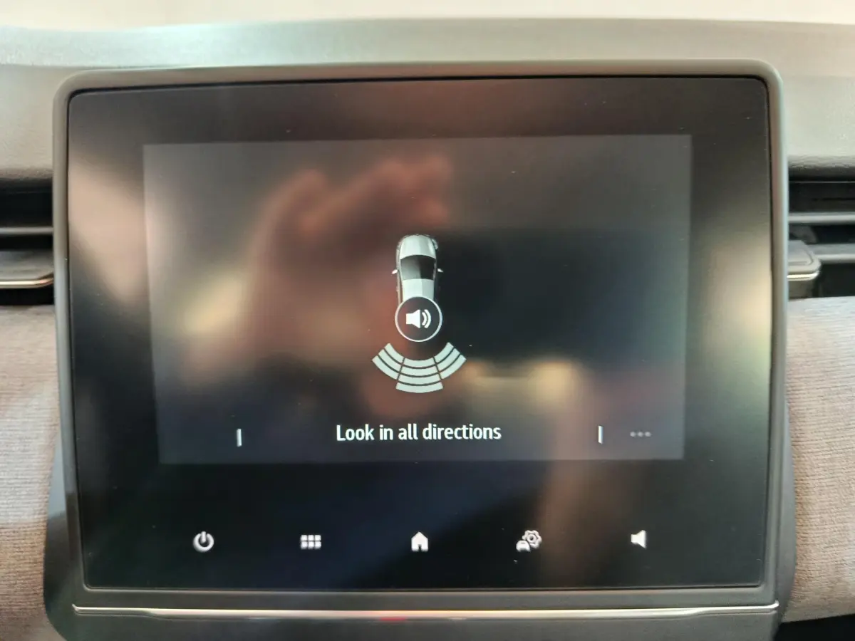 Écran tactile central de la Renault Clio noir affichant l'aide au stationnement avec vue du véhicule et alertes sonores.