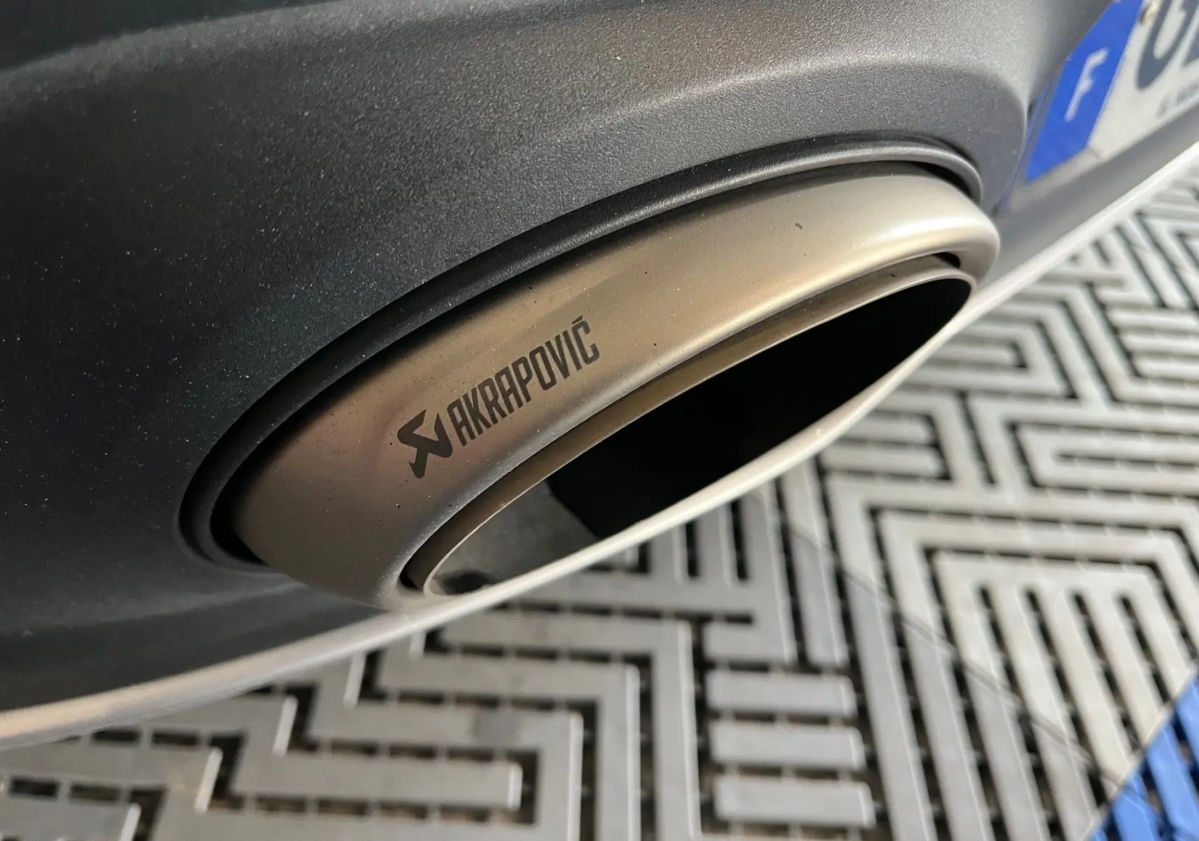 Gros plan sur la sortie d'échappement Akrapovic arrière droite d'une Porsche 911 992 Coupé argent GT sur sol à motifs.