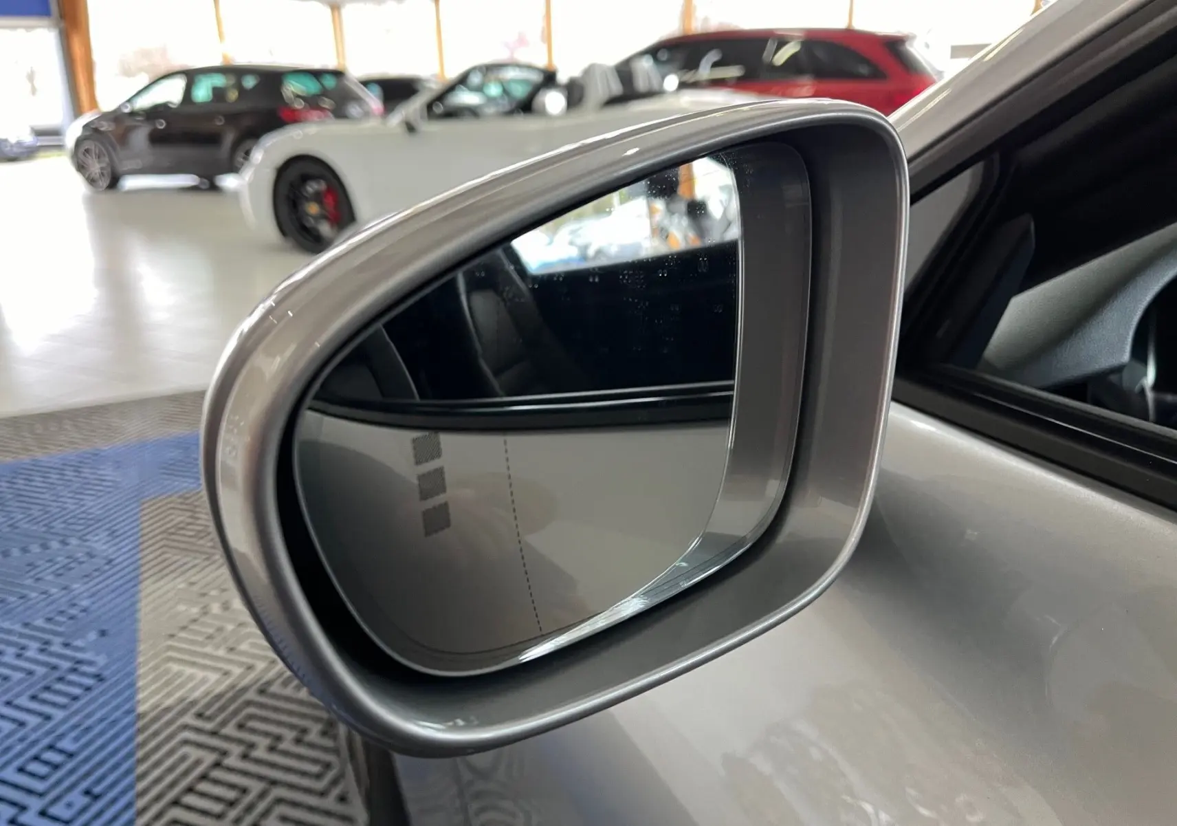 Rétroviseur côté gauche argent GT de la Porsche 911 (992) Carrera S en intérieur showroom avec autres voitures floues.