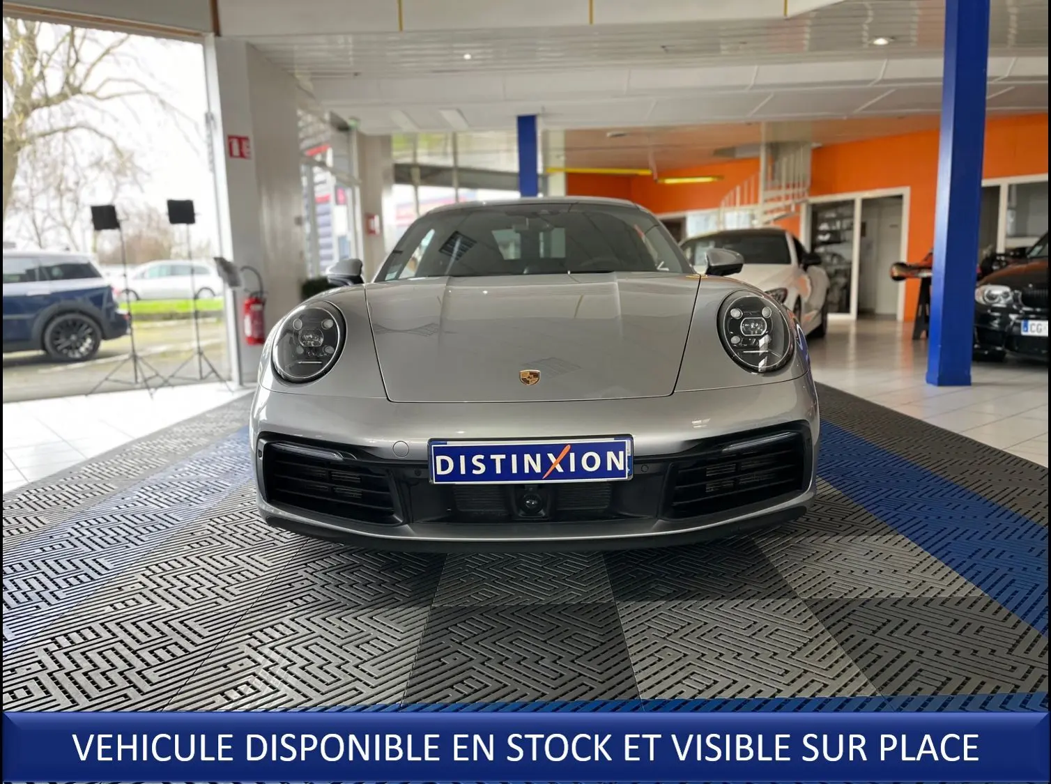 Vue frontale d'une Porsche 911 (992) Coupé argent GT exposée en showroom avec plaque Distinxion visible.