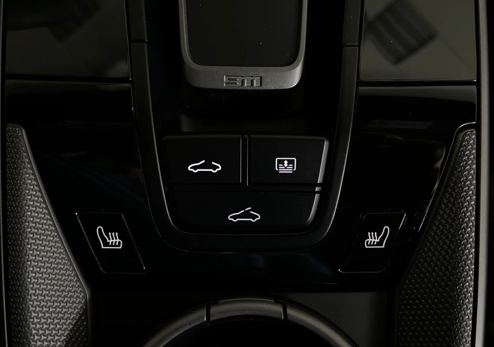 Gros plan sur la console centrale noire brillante de la Porsche 911 argent, avec boutons de toit ouvrant et sièges chauffants.