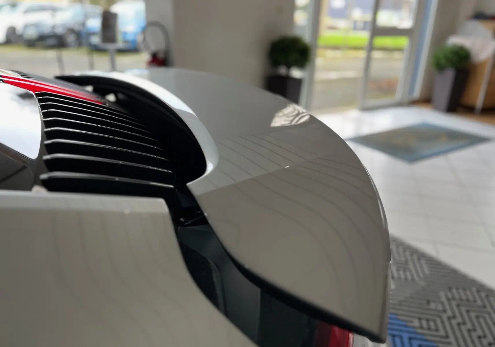 Gros plan sur l’aileron arrière relevé argent GT de la Porsche 911 (992) Carrera S dans un showroom lumineux.