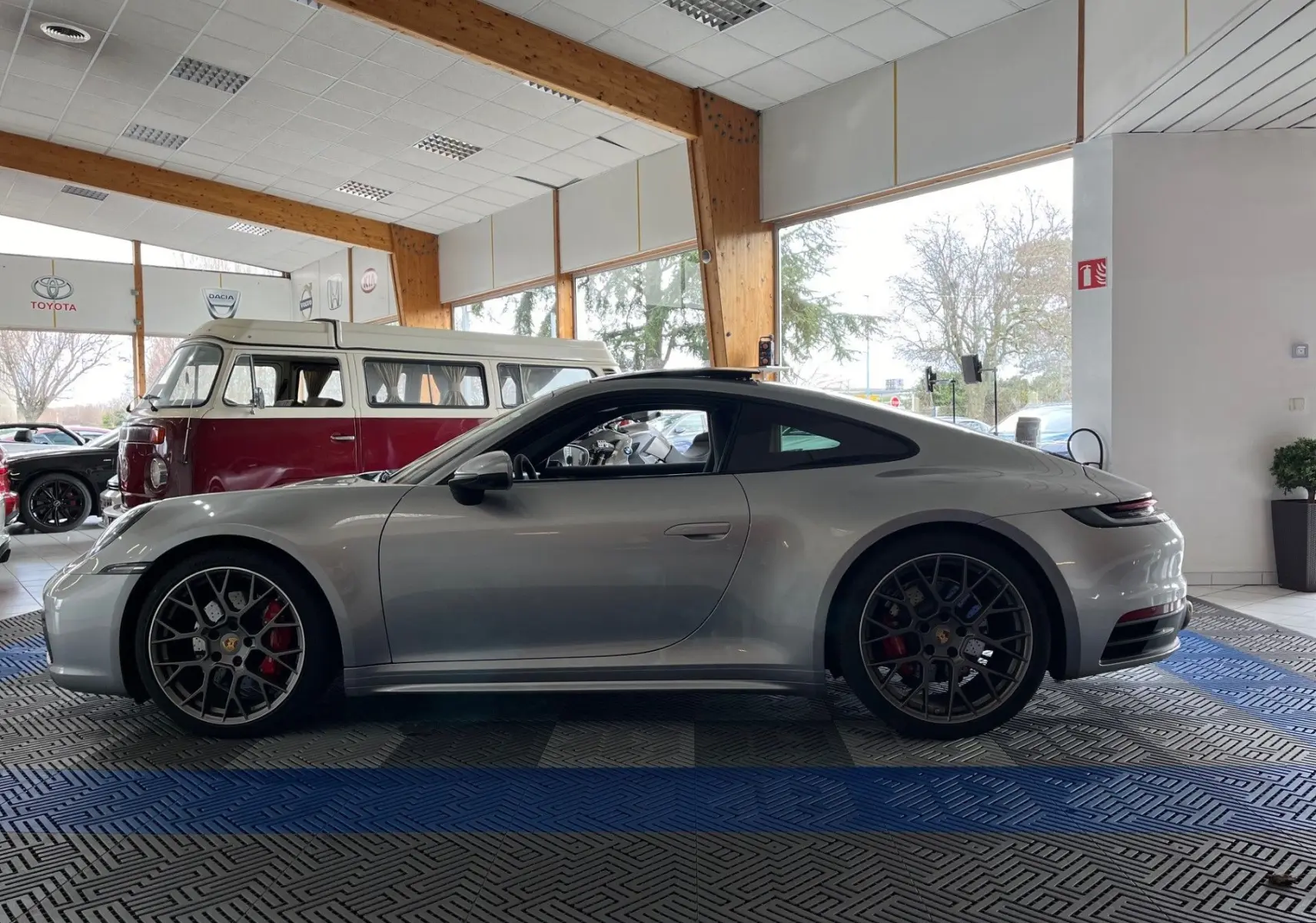 Profil côté gauche de la Porsche 911 Carrera S 2019 en argent GT avec jantes RS Spyder et intérieur noir visible en showroom.