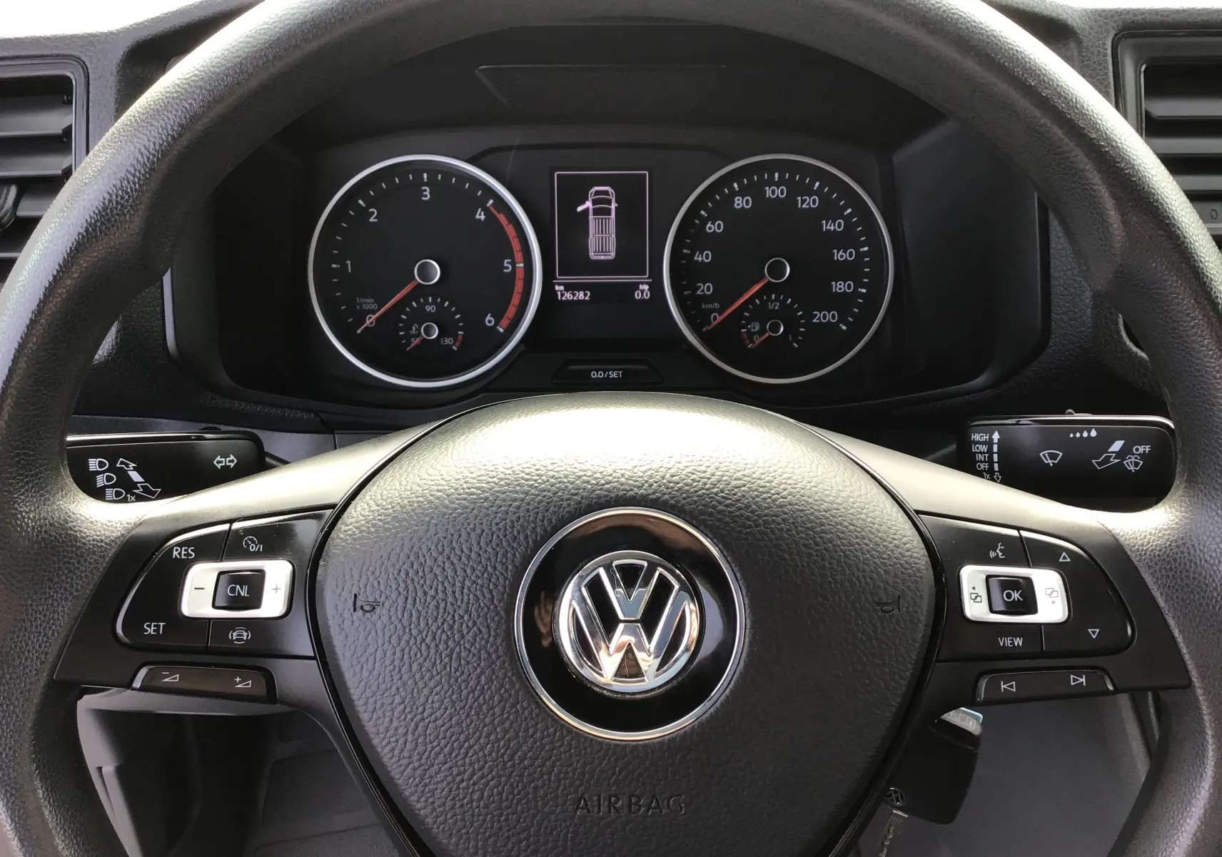 Vue rapprochée du volant multifonction noir avec logo Volkswagen et tableau de bord numérique du Crafter Fourgon blanc 2021.