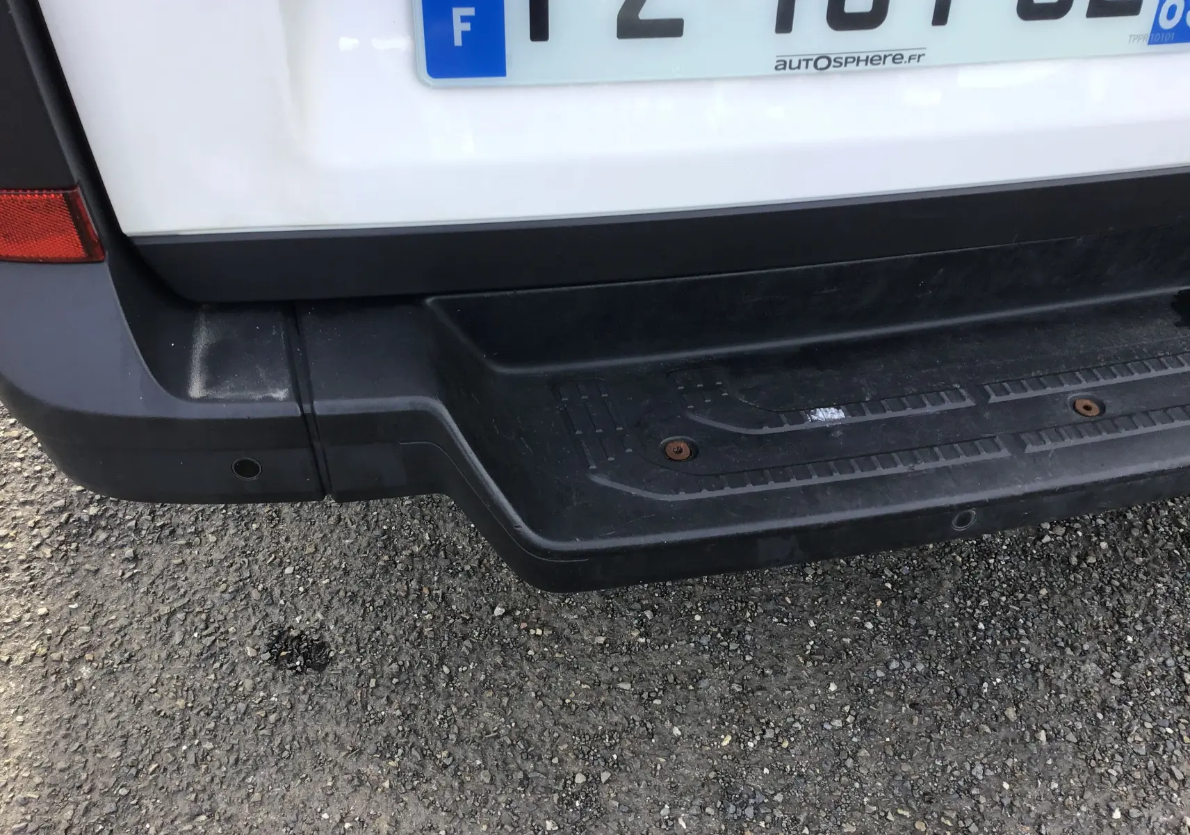 Gros plan sur le pare-chocs arrière noir et la plaque d'immatriculation d'un Volkswagen Crafter blanc.