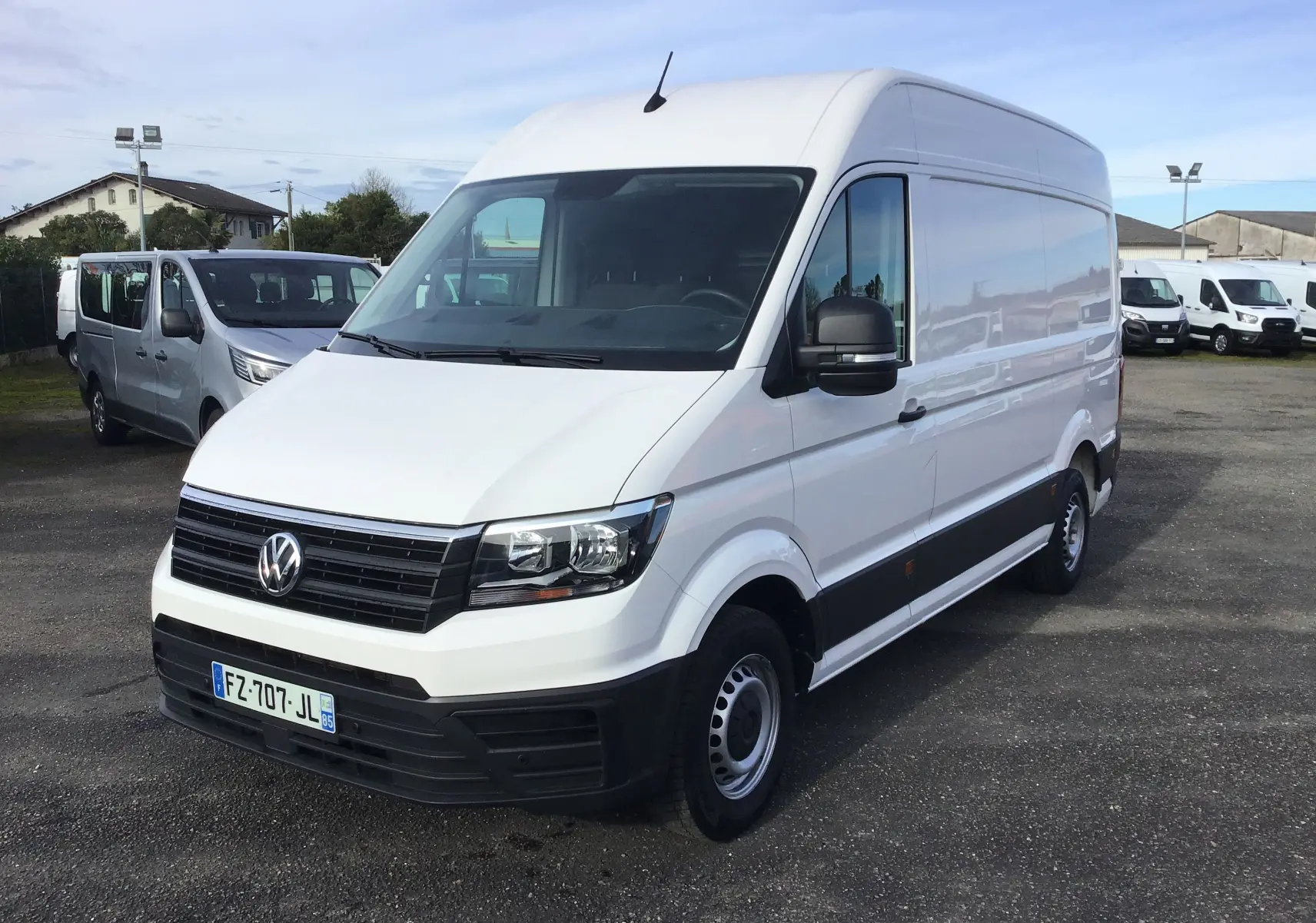 Vue 3/4 avant d'un Volkswagen Crafter fourgon blanc, avec calandre noire et jantes acier, stationné sur un parking extérieur.