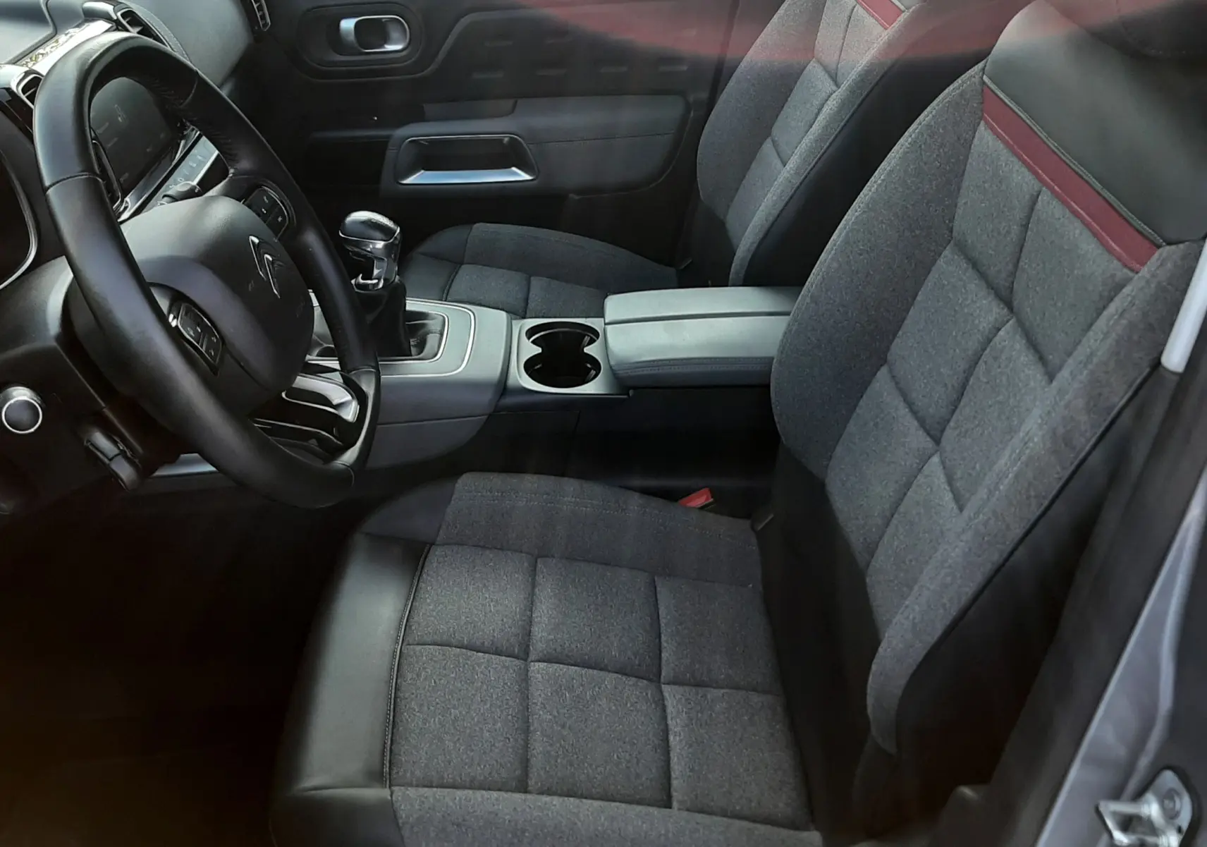 Intérieur avant du Citroën C5 Aircross gris, sièges tissu gris avec bande rouge, volant, levier de vitesse manuel visible.