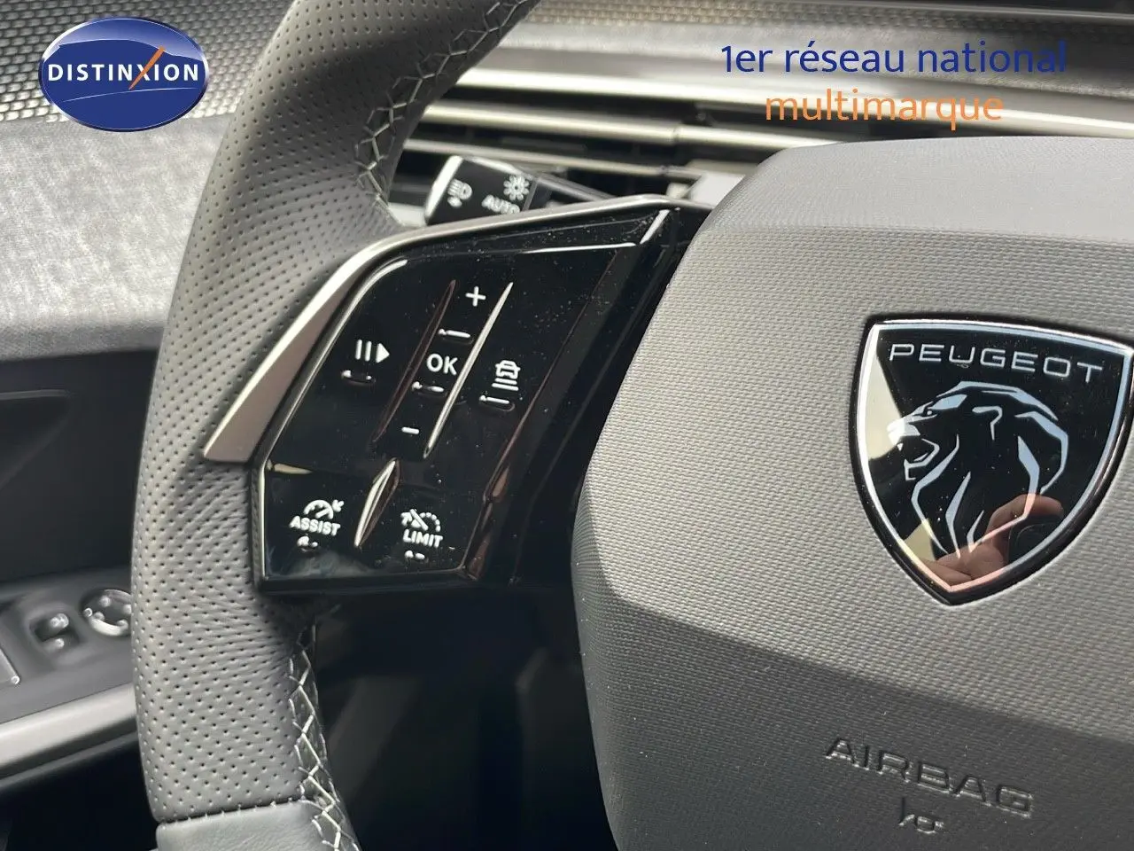 Gros plan sur le volant perforé gris avec commandes intégrées et logo Peugeot du SUV 5008 hybride 2025.