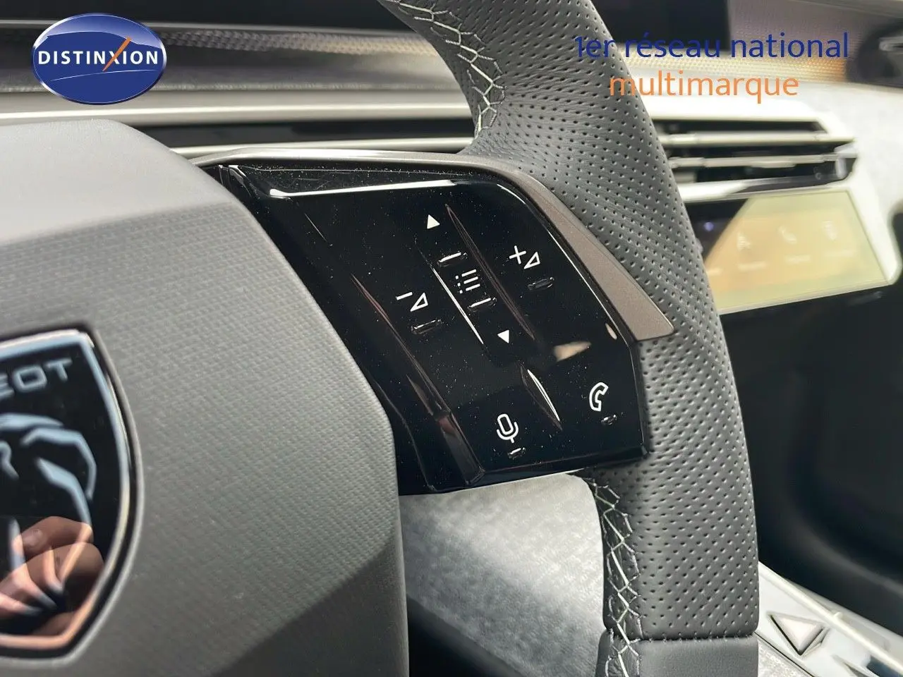 Gros plan sur le volant en cuir perforé gris du Peugeot 5008 Hybrid 2025 avec commandes tactiles intégrées.