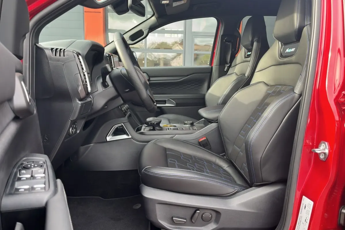 Vue intérieure côté conducteur du Ford Ranger 3.0 V6 240 MS-RT Plus rouge, sièges cuir noirs avec surpiqûres bleues.