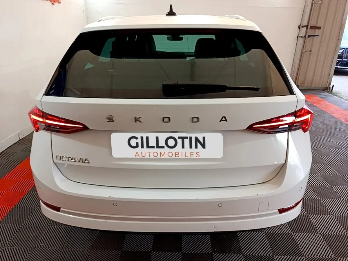 Vue arrière d'une Skoda Octavia blanche 2022 avec feux LED allumés et logo apparent sur un sol à damiers rouge et noir.