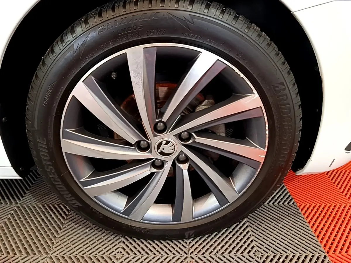 Gros plan sur la roue avant droite d’une Skoda Octavia blanche, jante alliage gris foncé à 5 doubles branches.