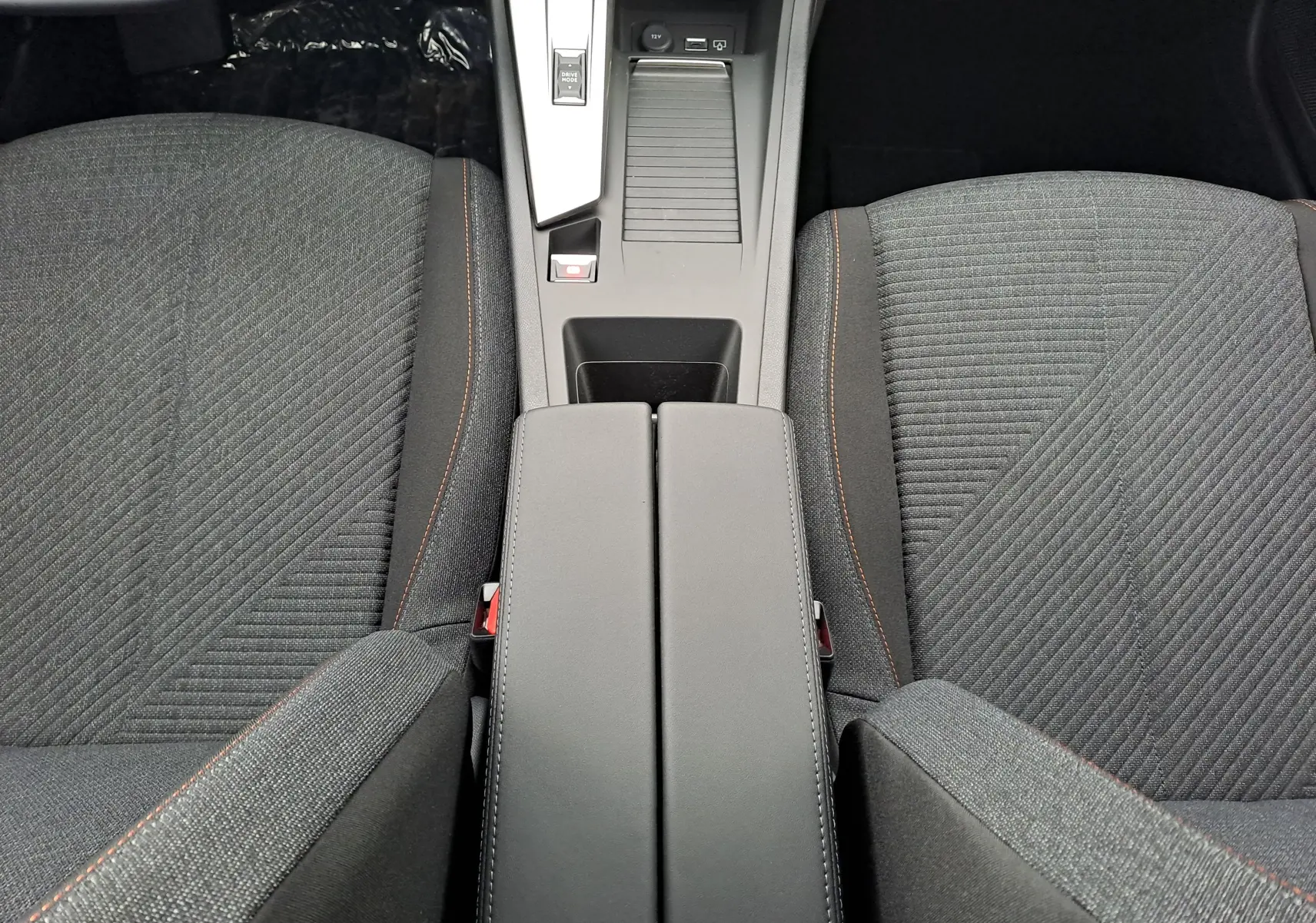 Vue plongeante sur la console centrale et les sièges avant en tissu gris avec surpiqûres orange du Peugeot 308 2025.