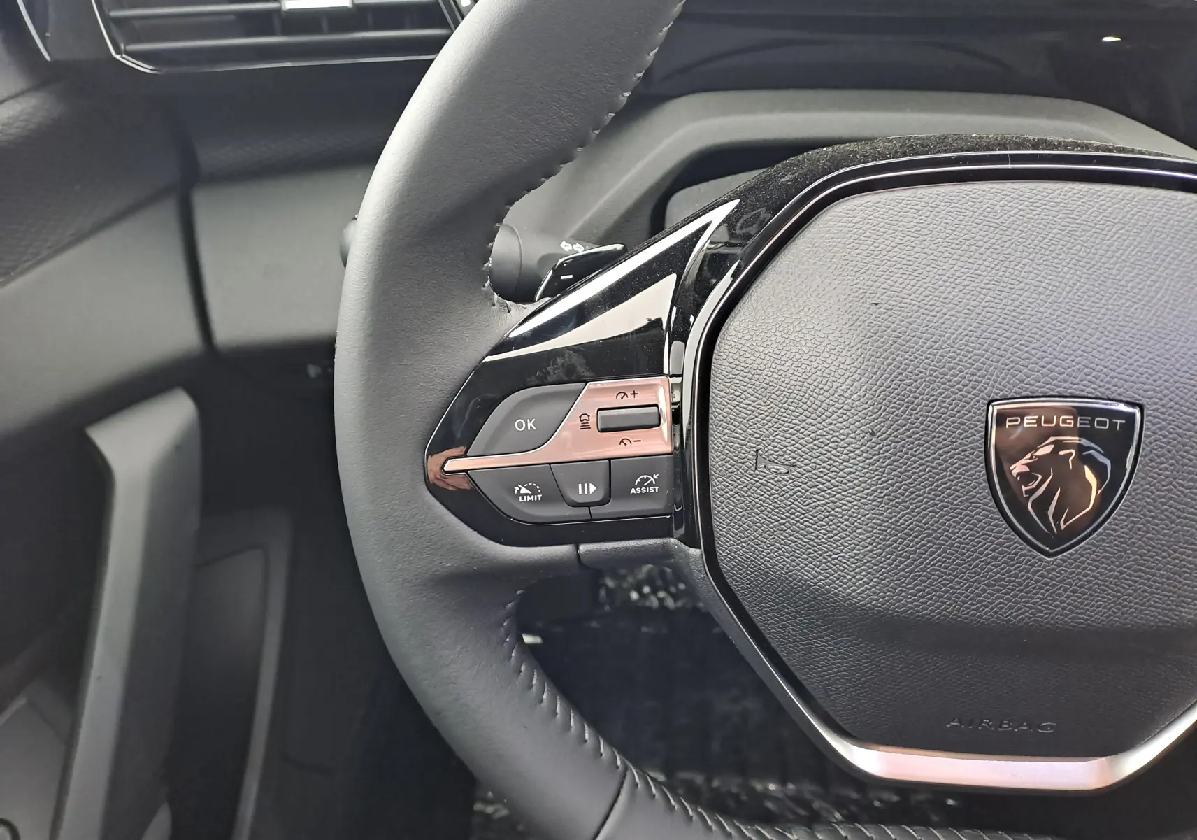 Gros plan sur le volant noir de la Peugeot 308 2025, avec commandes intégrées et logo lion chromé au centre.
